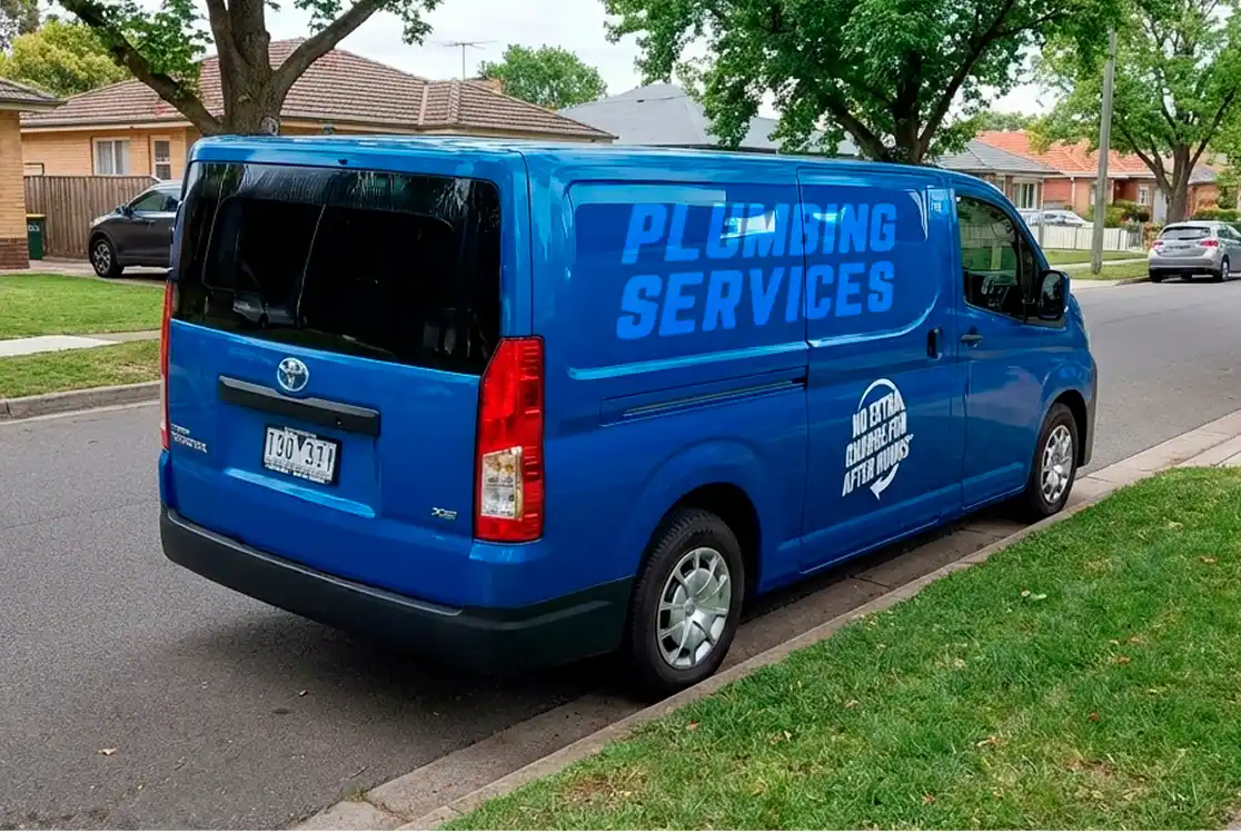Bright blue Toyota plumbing service van parked on a residential street, featuring "PLUMBING SERVICES" branding on the side panel and a "NO EXTRA CHARGE FOR AFTER HOURS" decal.